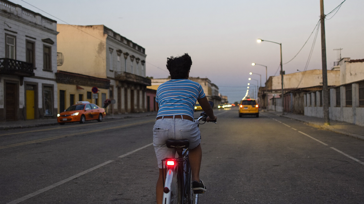 Ciclista en una calle de Lima al anochecer, con una luz roja pequeña en el tubo del asiento. Imagen ilustrativa generada por IA.
