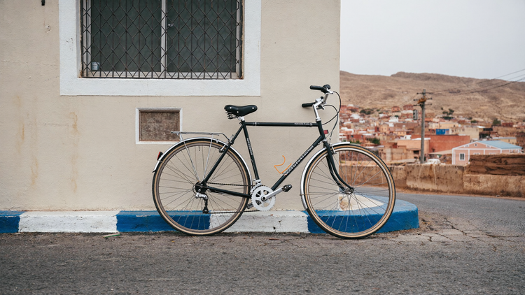 Bicicleta apoyada en una pared de una calle de Lima, con el asiento a la vista y cerros con casas al fondo