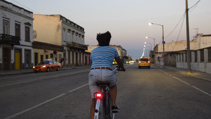 Ciclista en una calle de Lima al anochecer, con una luz roja pequeña en el tubo del asiento. Imagen ilustrativa generada por IA.